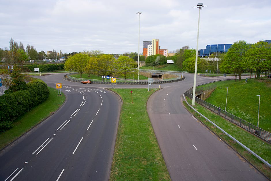 Roundabout with clear road markings surrounded by greenery and buildings in the background.