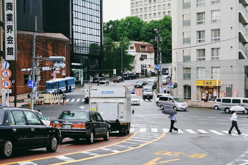 City street scene with various vehicles and pedestrians at a busy intersection.