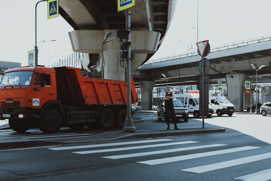 City intersection with red truck, pedestrian, and overpass in bright daylight.