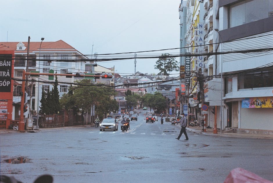 A pedestrian crosses a busy street in an urban setting with vehicles and buildings.