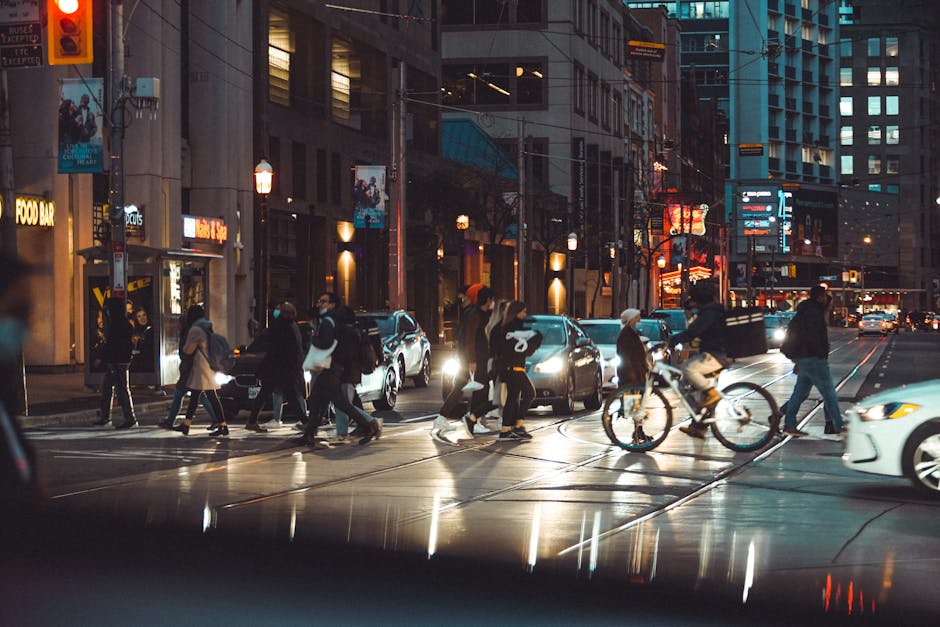 Urban evening scene with pedestrians and cyclists crossing a busy city intersection.